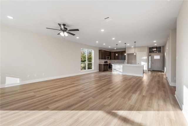 unfurnished living room featuring ceiling fan with notable chandelier and light hardwood / wood-style floors