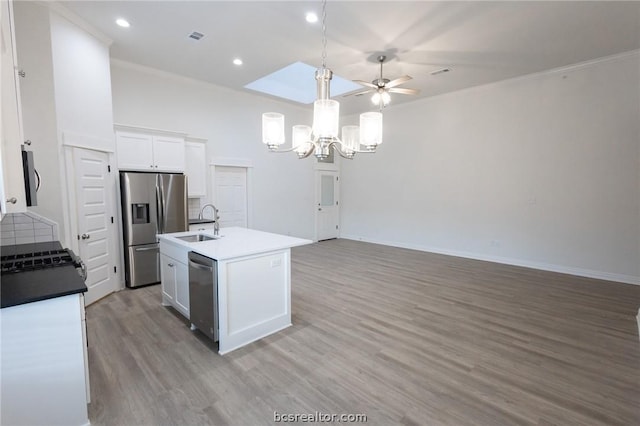 kitchen with white cabinets, ceiling fan with notable chandelier, an island with sink, appliances with stainless steel finishes, and light hardwood / wood-style floors