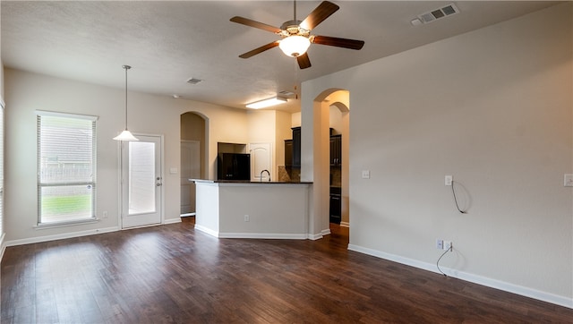 unfurnished living room with visible vents, arched walkways, dark wood-style floors, and a ceiling fan