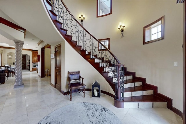 staircase featuring decorative columns, baseboards, marble finish floor, and a towering ceiling