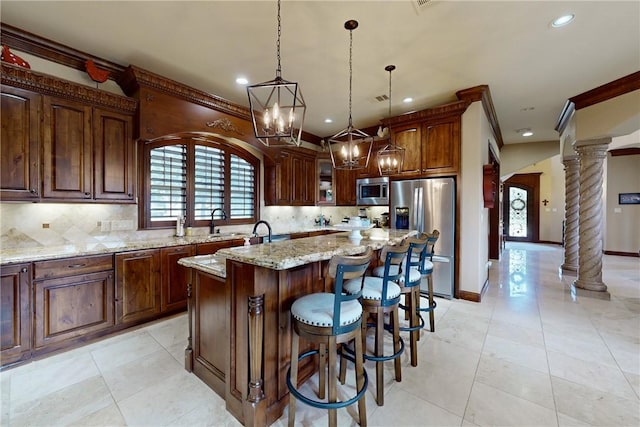 kitchen featuring light stone counters, backsplash, a center island, appliances with stainless steel finishes, and decorative columns