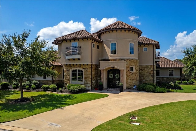 mediterranean / spanish house with a tile roof, stucco siding, a front yard, and a balcony