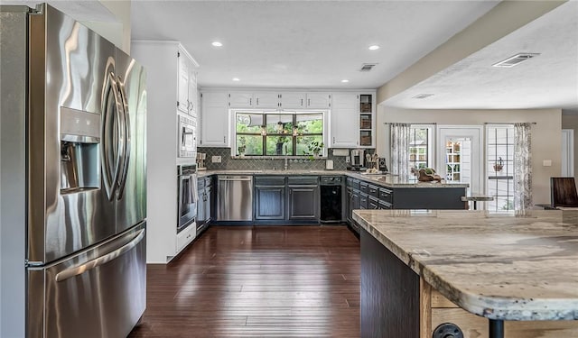 kitchen with kitchen peninsula, white cabinets, stainless steel appliances, and light stone counters