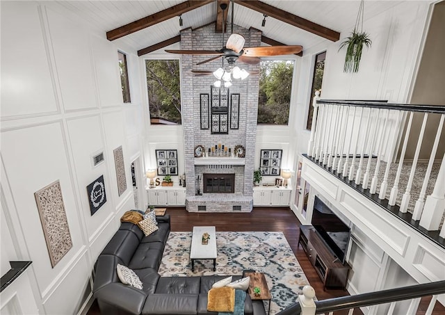 living room featuring a brick fireplace, ceiling fan, dark wood-type flooring, high vaulted ceiling, and beam ceiling