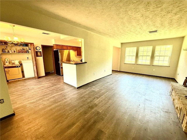 unfurnished living room featuring wood finished floors, visible vents, a notable chandelier, and a textured ceiling