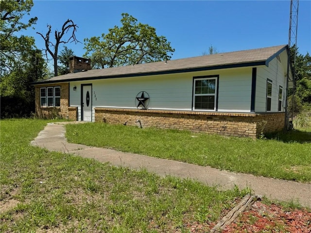 single story home featuring a chimney, brick siding, and a front yard