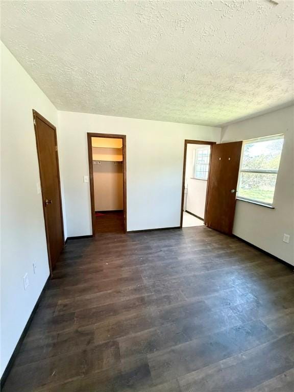 unfurnished bedroom with a textured ceiling, a spacious closet, dark wood finished floors, and baseboards