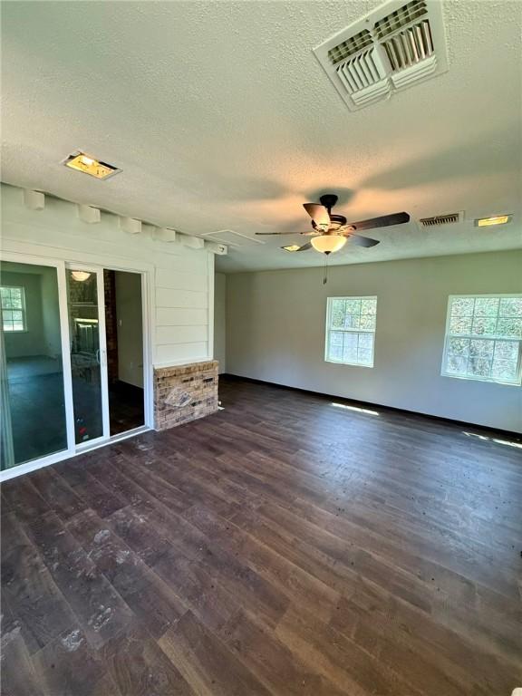 unfurnished living room featuring visible vents, ceiling fan, a textured ceiling, and dark wood-type flooring