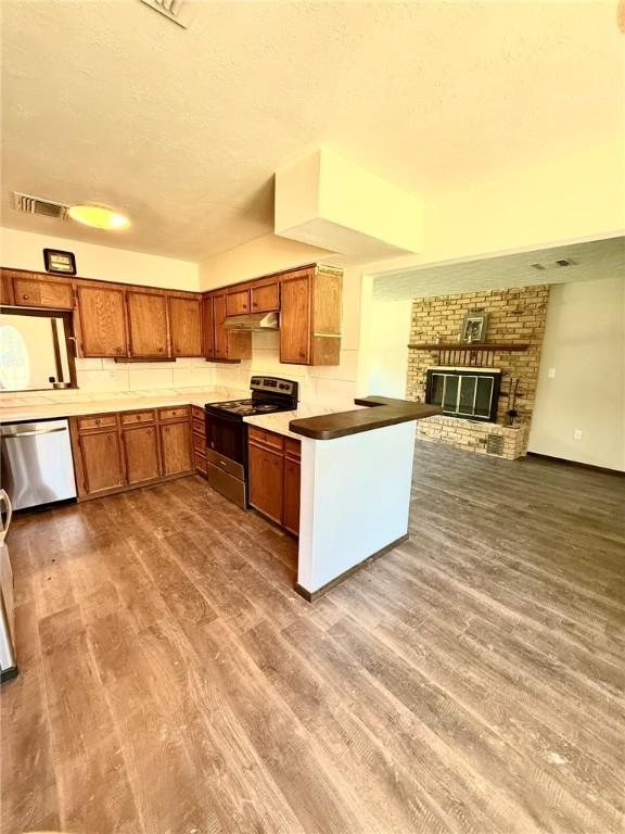 kitchen featuring under cabinet range hood, appliances with stainless steel finishes, brown cabinets, visible vents, and a peninsula
