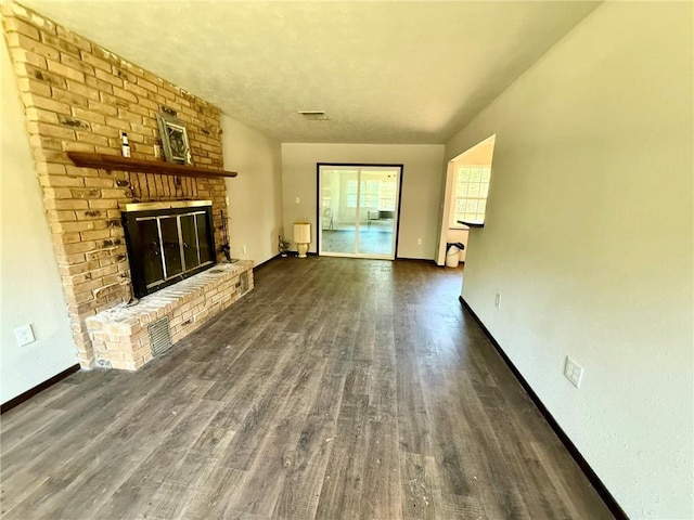 unfurnished living room featuring wood finished floors, baseboards, visible vents, and a brick fireplace