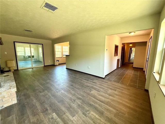 unfurnished living room featuring a textured ceiling, visible vents, baseboards, and dark wood-type flooring
