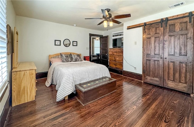 bedroom with ceiling fan, a barn door, and dark wood-type flooring