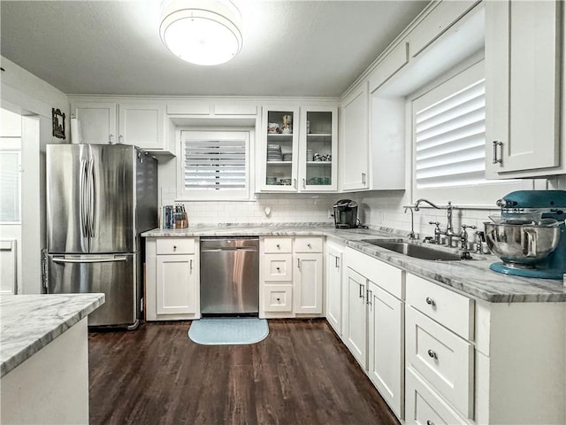 kitchen with light stone countertops, appliances with stainless steel finishes, dark wood-type flooring, sink, and white cabinetry