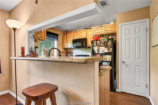 kitchen featuring kitchen peninsula, light brown cabinetry, a textured ceiling, black appliances, and dark hardwood / wood-style floors