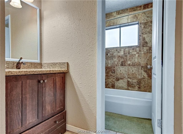 bathroom with a textured ceiling, vanity, and tiled shower / bath combo