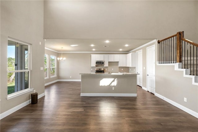 kitchen with white cabinetry, ornamental molding, an island with sink, dark hardwood / wood-style floors, and appliances with stainless steel finishes