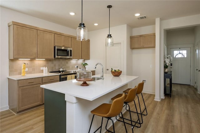 kitchen featuring appliances with stainless steel finishes, backsplash, a kitchen island with sink, light hardwood / wood-style floors, and hanging light fixtures