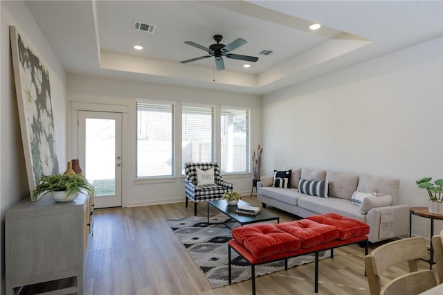 living room featuring ceiling fan, light hardwood / wood-style flooring, and a tray ceiling