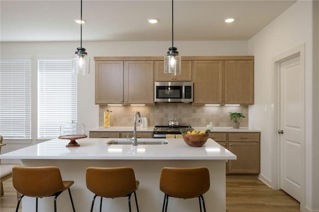 kitchen featuring sink, hanging light fixtures, stainless steel appliances, backsplash, and an island with sink