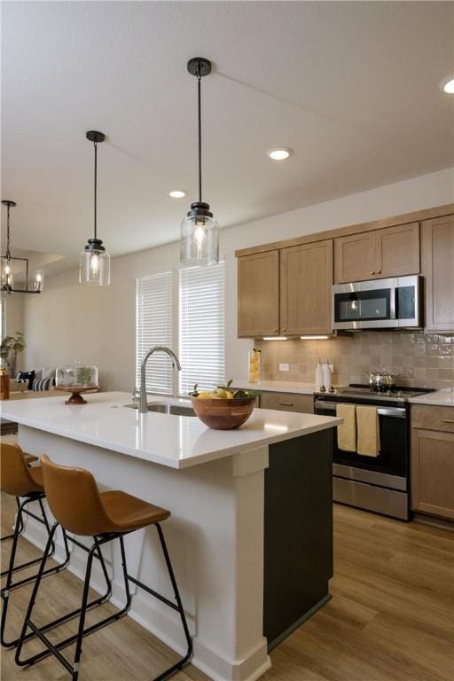 kitchen with pendant lighting, hardwood / wood-style floors, an island with sink, appliances with stainless steel finishes, and a kitchen bar