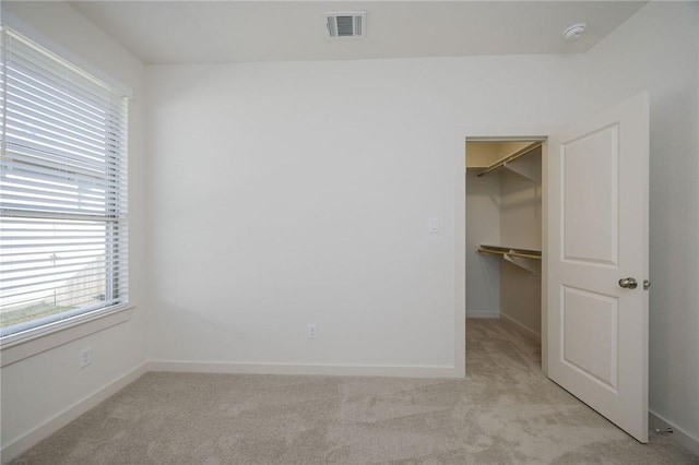 unfurnished bedroom with light colored carpet, a spacious closet, and a closet