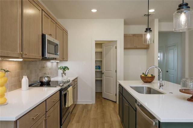 kitchen featuring sink, light hardwood / wood-style flooring, backsplash, pendant lighting, and appliances with stainless steel finishes