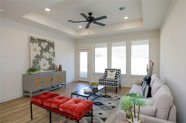 living room with ceiling fan, light hardwood / wood-style floors, and a tray ceiling