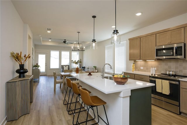 kitchen with pendant lighting, a center island with sink, light hardwood / wood-style flooring, ceiling fan, and appliances with stainless steel finishes