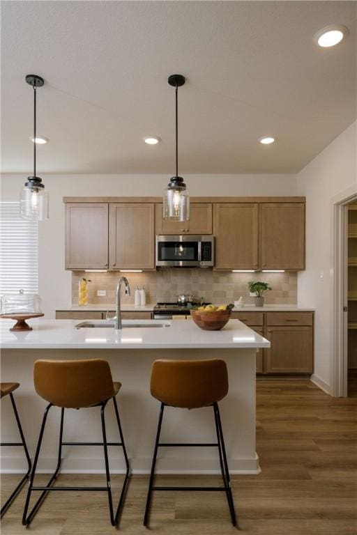 kitchen featuring sink, tasteful backsplash, hardwood / wood-style floors, decorative light fixtures, and appliances with stainless steel finishes