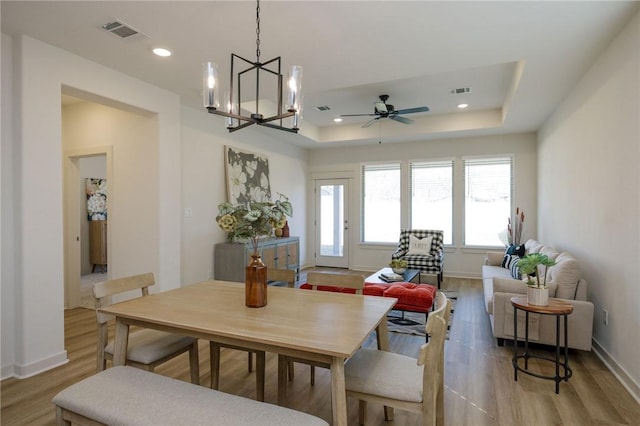 dining area featuring ceiling fan with notable chandelier, light hardwood / wood-style flooring, and a raised ceiling