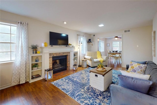 living area featuring visible vents, a ceiling fan, a brick fireplace, and wood finished floors
