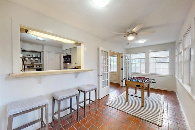 recreation room featuring dark tile patterned flooring, a ceiling fan, baseboards, and french doors