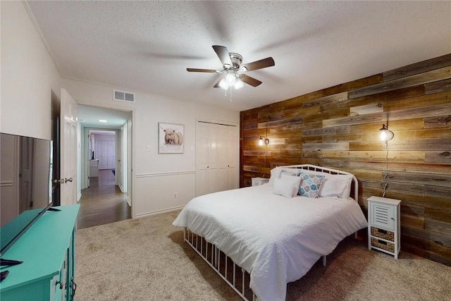 carpeted bedroom featuring ceiling fan, a textured ceiling, visible vents, wood walls, and a closet