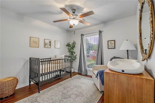 bedroom featuring dark hardwood / wood-style flooring, a nursery area, and ceiling fan