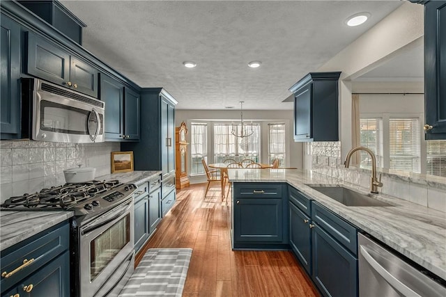 kitchen with sink, stainless steel appliances, dark hardwood / wood-style floors, decorative light fixtures, and kitchen peninsula