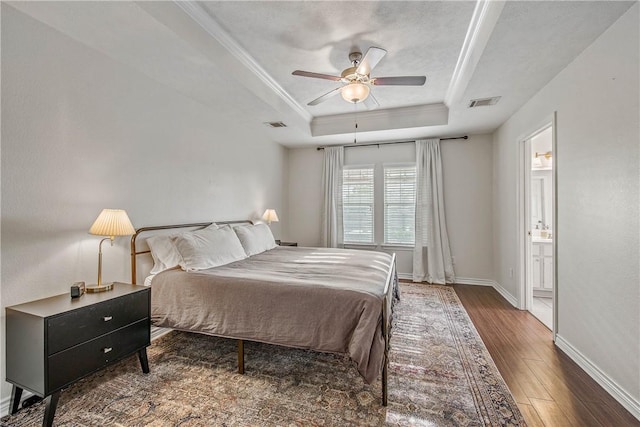 bedroom with crown molding, ceiling fan, ensuite bathroom, dark hardwood / wood-style flooring, and a raised ceiling