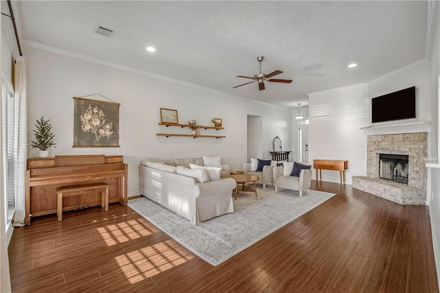 living room with ceiling fan, crown molding, a fireplace, and wood-type flooring