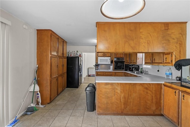 kitchen with light tile patterned floors, brown cabinetry, a peninsula, a sink, and black appliances