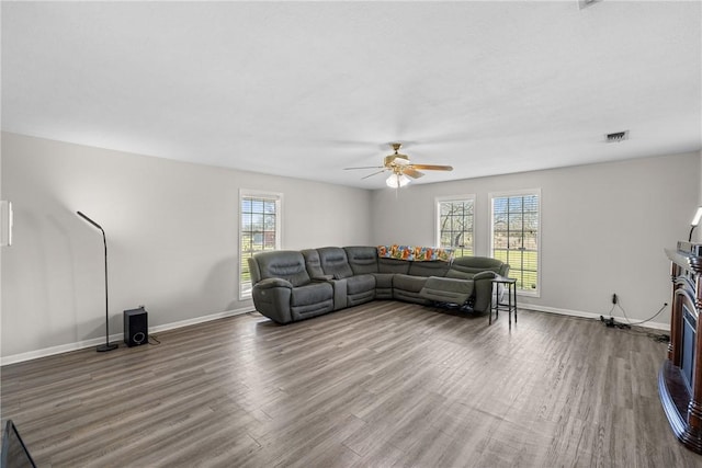 living area featuring a ceiling fan, wood finished floors, baseboards, and a fireplace