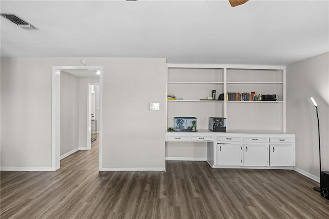 interior space with dark wood finished floors, visible vents, built in study area, and baseboards