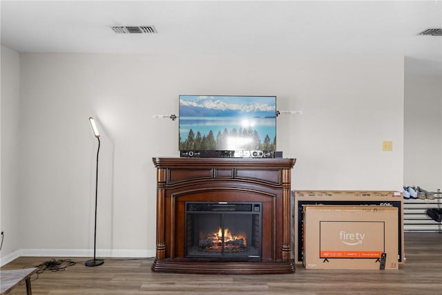 room details featuring visible vents, baseboards, a lit fireplace, and wood finished floors