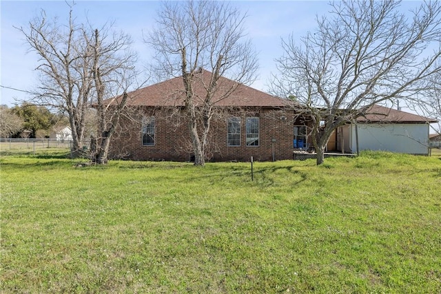 rear view of house featuring brick siding, a lawn, and fence