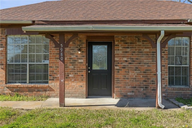 doorway to property featuring brick siding and roof with shingles