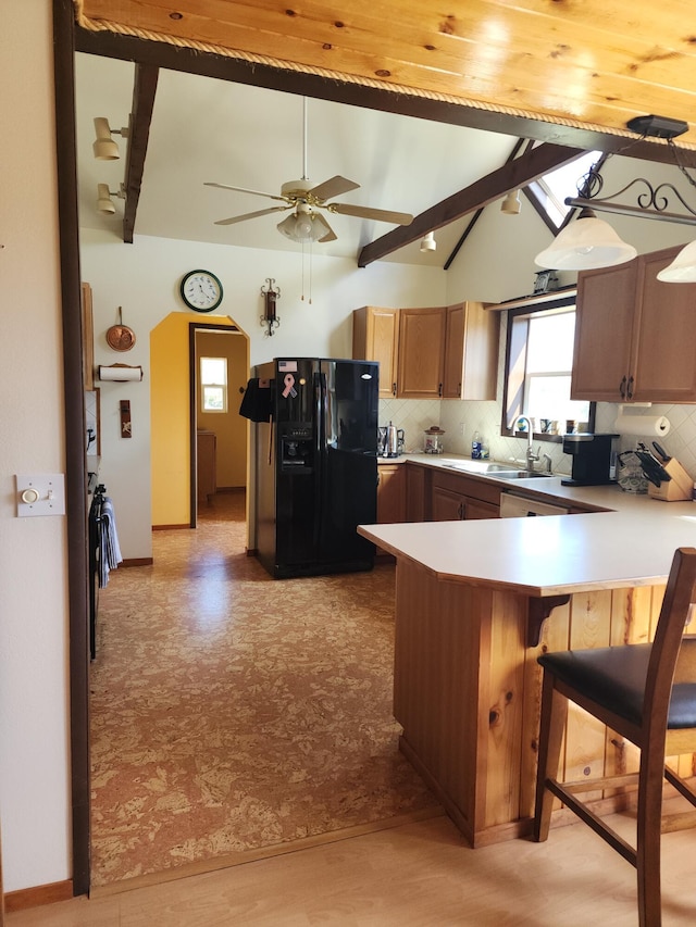 kitchen featuring vaulted ceiling with beams, a peninsula, light countertops, brown cabinets, and black refrigerator with ice dispenser