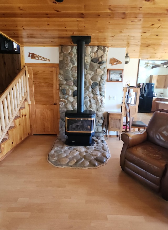 living room featuring a wood stove, wooden ceiling, light wood finished floors, and stairs