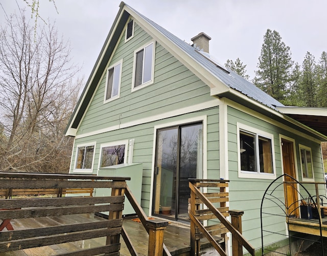 rear view of house featuring solar panels, a wooden deck, metal roof, and a chimney