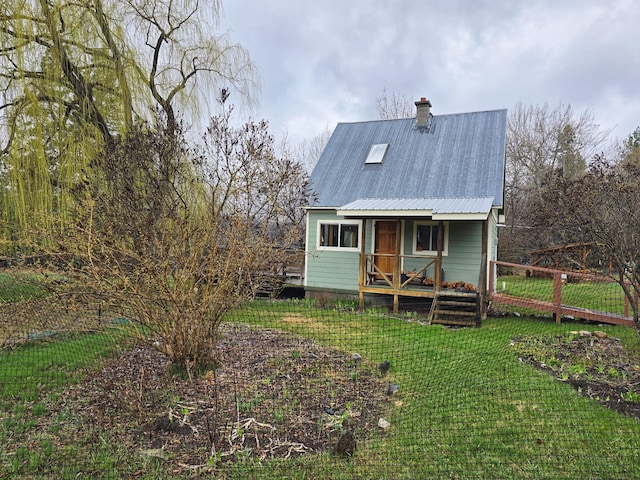 rear view of property featuring a lawn, a chimney, metal roof, and a porch