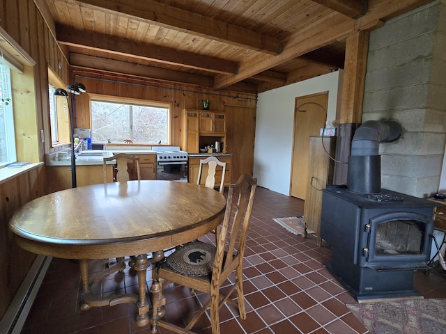 dining area with dark tile patterned floors, a wood stove, wood walls, wooden ceiling, and beamed ceiling