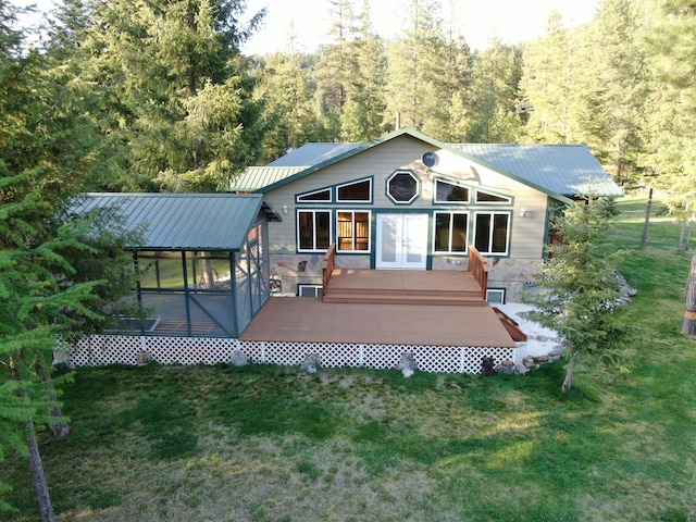 back of property with stone siding, a deck, french doors, metal roof, and a lawn