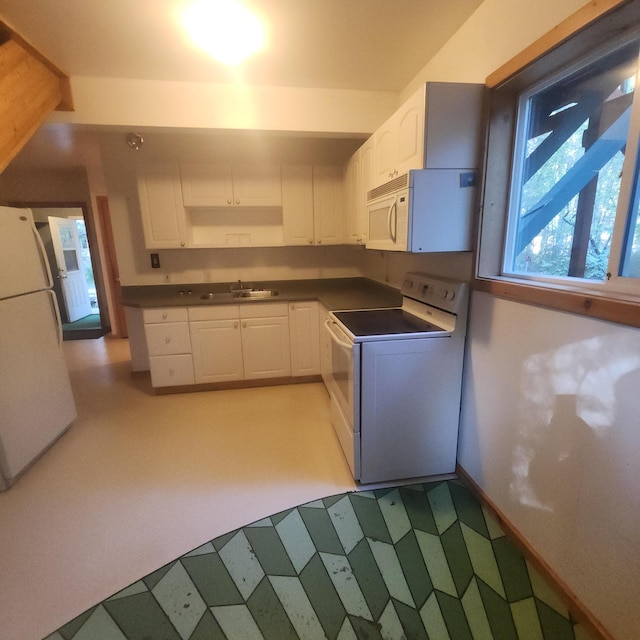 kitchen with a sink, white appliances, white cabinetry, baseboards, and dark countertops